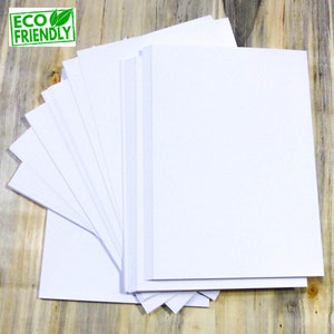 May include: A stack of white paper sheets, arranged in a fan shape, on a wooden surface. The paper is eco-friendly.