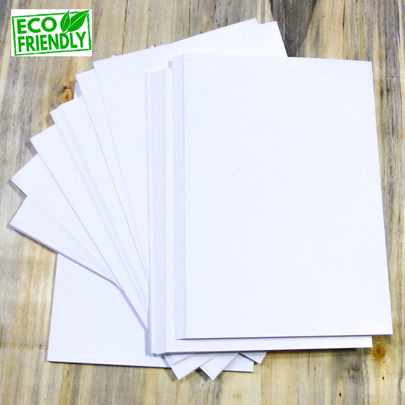 May include: A stack of white paper sheets, arranged in a fan shape, on a wooden surface. The paper is eco-friendly.