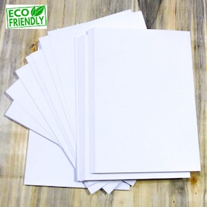 May include: A stack of white paper sheets, arranged in a fan shape, on a wooden surface. The paper is eco-friendly.