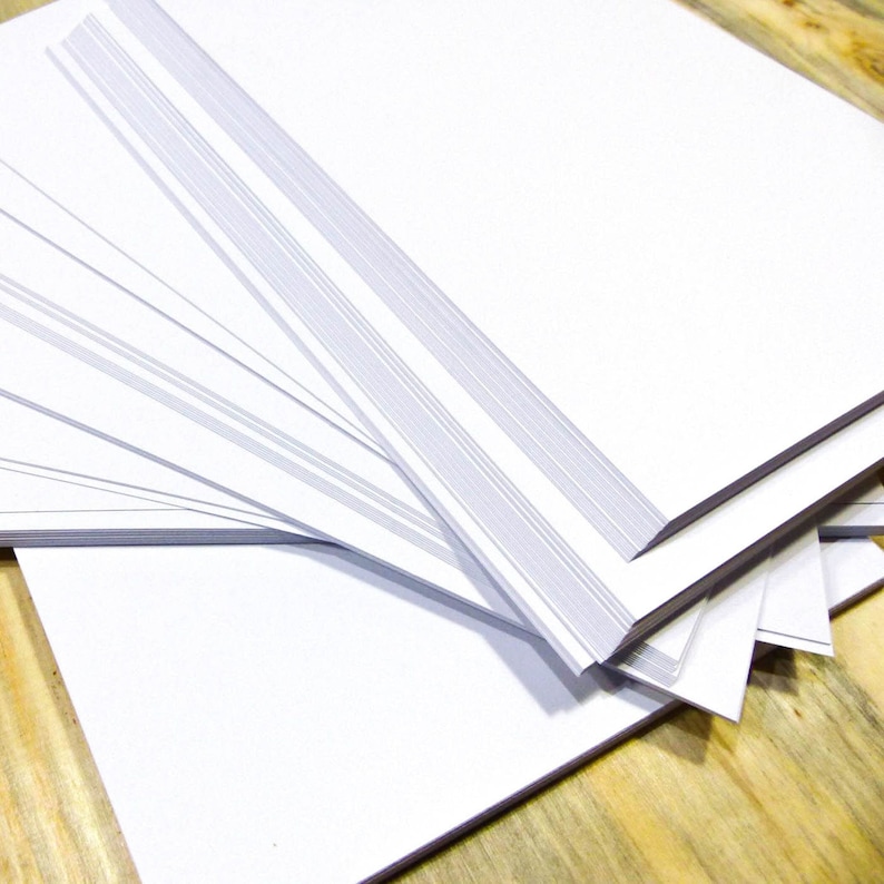 May include: A stack of white paper sheets, neatly arranged and fanned out, with the edges of the sheets visible. The paper is smooth and clean, suggesting a new pack of paper.
