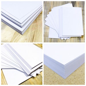 May include: Four stacks of white cardstock paper on a wooden surface. The stacks are arranged in different configurations, showing the paper's smooth texture and crisp edges.