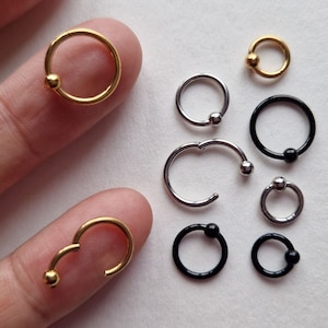 May include: Assortment of gold, silver, and black hoop earrings with ball closures. The hoops are different sizes and styles, including a few with a curved shape.