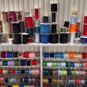 May include: A variety of spools of colorful thread are organized on shelves. The spools are arranged by color, with each shelf containing a different color group. The thread is likely used for crafting or sewing.