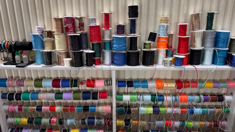 May include: A variety of spools of colorful thread are organized on shelves. The spools are arranged by color, with each shelf containing a different color group. The thread is likely used for crafting or sewing.