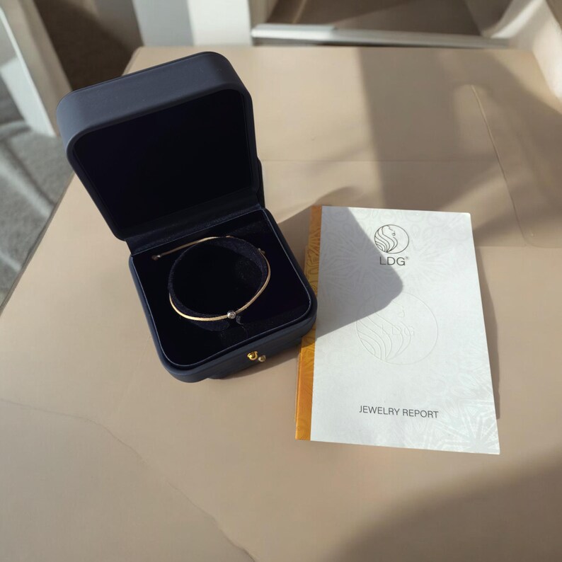 May include: A gold bracelet with a small black bead in a black velvet jewelry box with a white card that says "LDG" and "Jewelry Report".