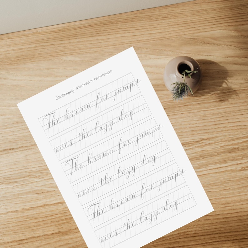 K&ouml;nnte beinhalten: Ein Kalligraphie-Arbeitsblatt mit grauen Linien und dem Text "The brown fox jumps over the lazy dog", der dreimal wiederholt wird.