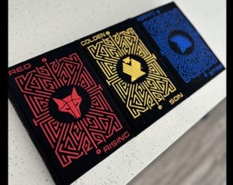May include: Three hardback books with black covers and colourful maze patterns. The titles are "Red Rising", "Golden Son", and "Morning Star".