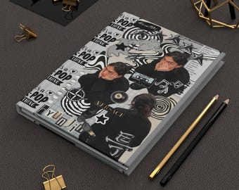 Puede incluir: Un diario con un diseño de collage que presenta a una persona, cintas de cassette y el texto "It's a POP thing" en blanco y negro. El diario está junto a lápices dorados y negros y clips dorados.