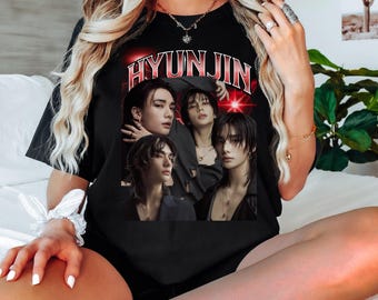 May include: Black t-shirt with a graphic of four people and the name "HYUNJIN" in red. The design has a vintage, faded appearance. The shirt is a crew neck and looks to be made of a soft material.