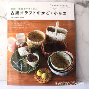 May include: A book cover with the title "Old Paper Craft Baskets and Small Items" in Japanese. The cover features a variety of woven baskets and bowls made from recycled paper, including a small bowl with apples inside.