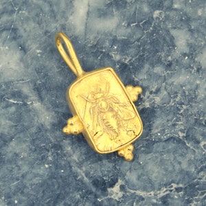 May include: Gold pendant featuring a detailed bee design, set in a rectangular frame with decorative accents.