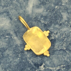 May include: Gold pendant with a rectangular shape and a smooth, polished finish. The pendant has four small, decorative accents on the edges.