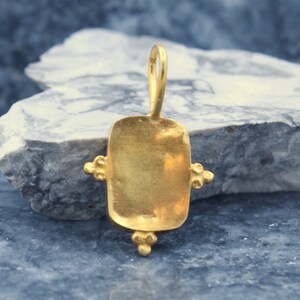 May include: Gold pendant with a rectangular shape and a smooth surface. The pendant has four small decorative accents on the edges.