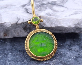 May include: A gold pendant with a green glass lion head cameo and a green gemstone accent.