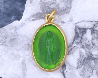 May include: A gold-toned oval pendant with a green glass inset featuring a depiction of the Virgin Mary. The inscription around the edge reads "Miraculous Medal".