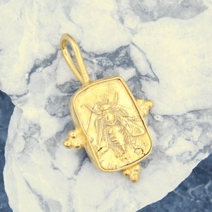 May include: Gold pendant featuring a detailed bee design. The pendant is rectangular with a textured surface and has a loop at the top for attaching to a chain.