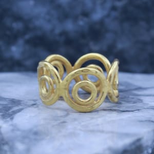 May include: Gold ring with a swirling, circular design. The ring is made of a thick, textured metal.