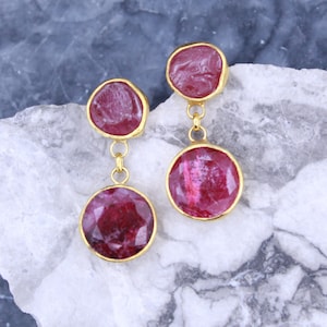 May include: A pair of dangle earrings with two round, faceted, pink gemstones on each earring. The gemstones are connected by a gold chain.