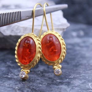 May include: A pair of gold earrings with oval-shaped amber stones and a small diamond accent on each earring.