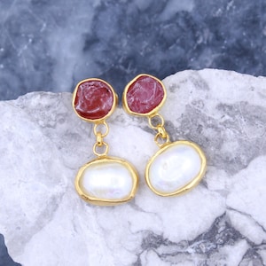 May include: Gold earrings with a red cameo and a white pearl drop. The earrings are on a gray and white background.