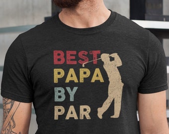 May include: Dark gray t-shirt with the text "BEST PAPA BY PAR" in red, yellow, and blue. A beige silhouette of a golfer swinging a club is next to the text. The shirt is made of a soft material.