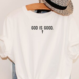 May include: White t-shirt with the text "GOD IS GOOD." and a small cross symbol below the text.