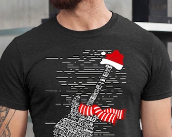 May include: Dark gray t-shirt featuring a white guitar graphic composed of musical terms. The guitar is adorned with a Santa hat and a red and white striped scarf, suggesting a Christmas theme. The shirt is a casual wear item.