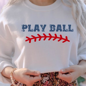 May include: White sweatshirt with the text "PLAY BALL" in blue with a red baseball stitch graphic.