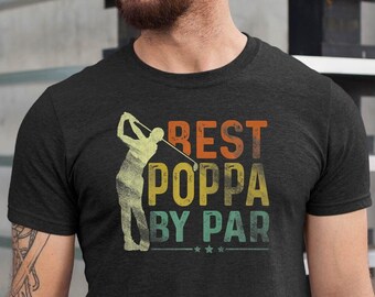 May include: A dark grey t-shirt with a vintage-style graphic of a golfer swinging a club. The text "BEST POPPA BY PAR" is printed in colorful letters on the shirt.