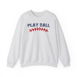 May include: A gray sweatshirt with the text "PLAY BALL" in blue and red stitching on the front.