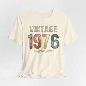 May include: A vintage-style t-shirt with the text "Vintage 1976 Original Parts" in a distressed font. The numbers are in a rainbow color scheme.
