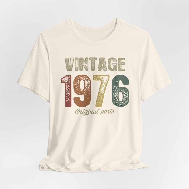 May include: A vintage-style t-shirt with the text "Vintage 1976 Original Parts" in a distressed font. The numbers are in a rainbow color scheme.