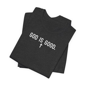 May include: A dark gray t-shirt with the text "GOD IS GOOD." in white lettering and a white cross symbol.