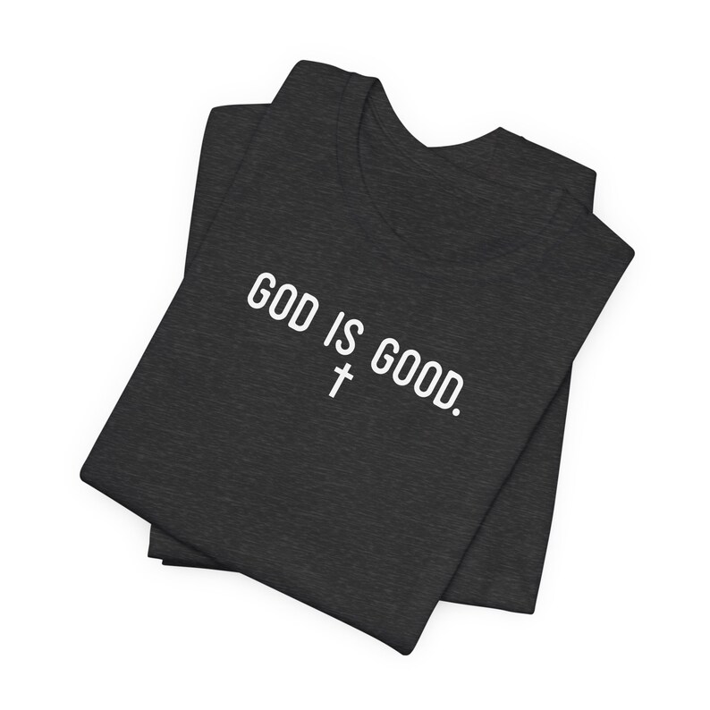 May include: A dark gray t-shirt with the text "GOD IS GOOD." in white lettering and a white cross symbol.