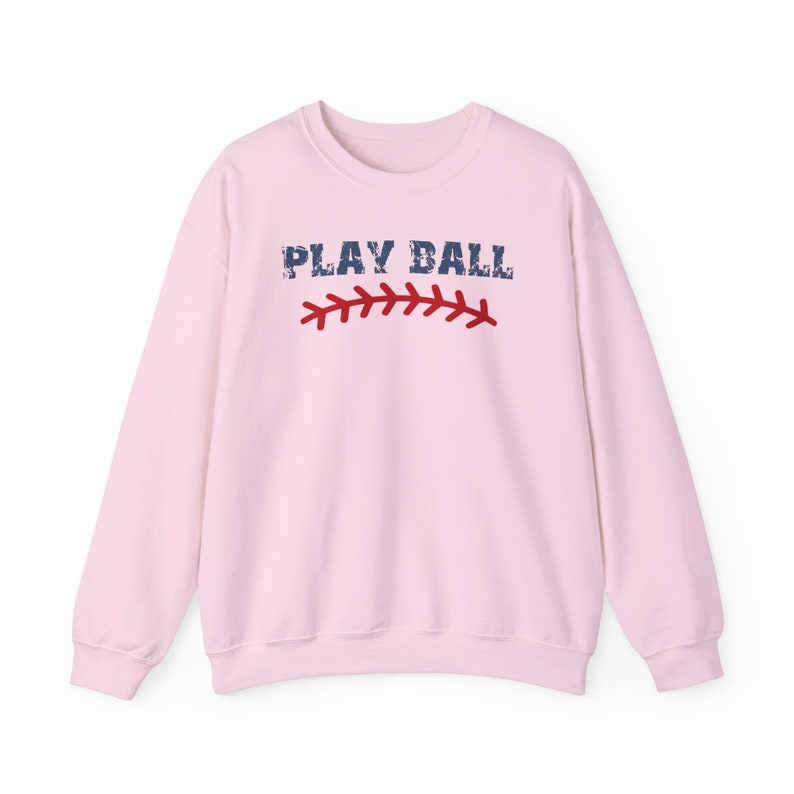 May include: Pink sweatshirt with the text "PLAY BALL" in blue with a red baseball stitch graphic.