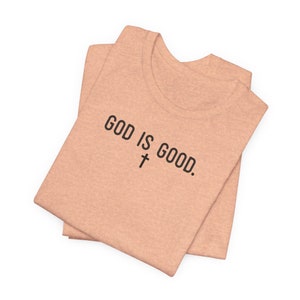 May include: A folded peach-colored t-shirt with the text "GOD IS GOOD." and a cross symbol printed on the front.