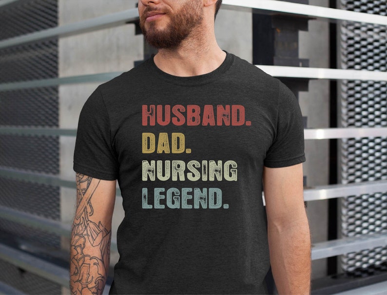 May include: A dark grey t-shirt with the text "Husband. Dad. Nursing Legend." printed in white with a vintage style font.