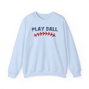 May include: Light blue sweatshirt with the text "PLAY BALL" in navy blue with a red baseball stitch graphic.