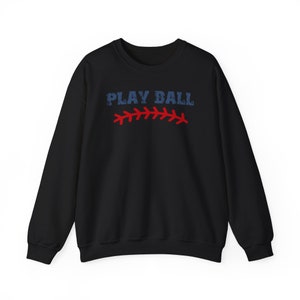 May include: Black sweatshirt with the text "PLAY BALL" in blue and red stitching. The stitching resembles a baseball seam.
