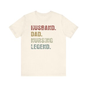 May include: A light beige t-shirt with the text "Husband. Dad. Nursing Legend." in a vintage style font with red, green, and blue colors.