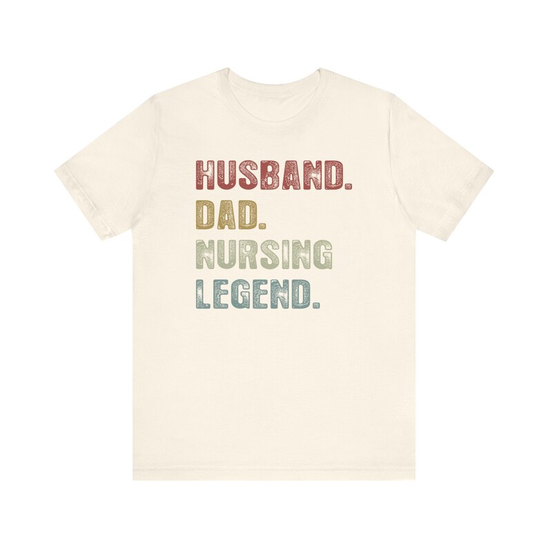 May include: A light beige t-shirt with the text "Husband. Dad. Nursing Legend." in a vintage style font with red, green, and blue colors.