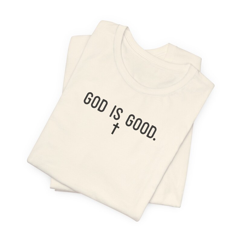May include: A folded white t-shirt with the text "GOD IS GOOD." and a cross symbol printed on the front.