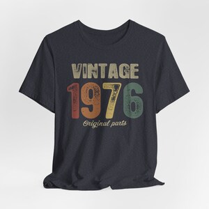 May include: A dark blue t-shirt with a vintage-style graphic that says "Vintage 1976 Original Parts". The numbers are in a rainbow color scheme.