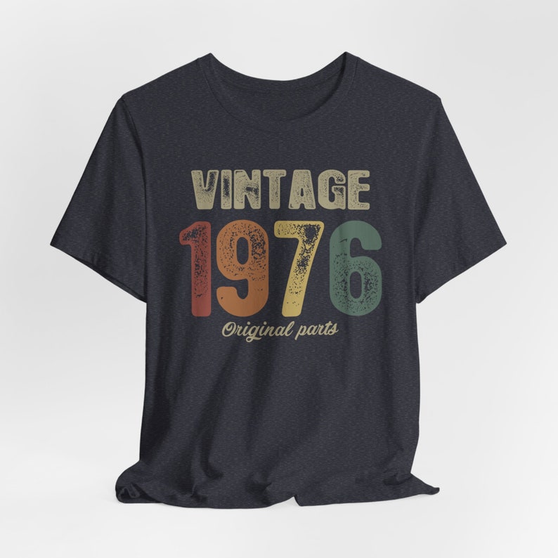 May include: A dark blue t-shirt with a vintage-style graphic that says "Vintage 1976 Original Parts". The numbers are in a rainbow color scheme.