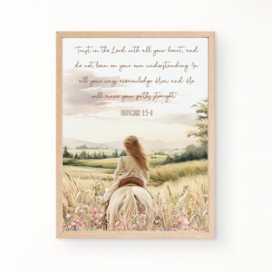 May include: A framed print featuring a watercolor illustration of a girl riding a white horse through a field of wildflowers. The artwork includes the text "Trust in the Lord with all your heart... Proverbs 3:5-6" in a script font. The frame is a light wood color.