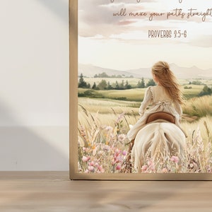 May include: A framed watercolor print depicts a young person riding a white horse through a field of tall grass and wildflowers. The artwork has a soft, pastel color palette with text from Proverbs 3:5-6.