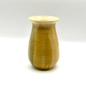Puede incluir: Un jarrón de cerámica hecho a mano con un borde ancho y ligeramente ensanchado y un cuerpo redondeado. El jarrón tiene una superficie texturizada con líneas horizontales y un degradado de color beige, verde oliva y marrón. El jarrón mide unos 18 cm de alto.