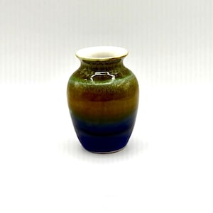 May include: A small ceramic vase with a rounded body and a narrow neck. The glaze features a gradient transition from a deep blue at the base to a warm brown in the middle, ending in a mossy green at the top rim. The interior of the rim is white.