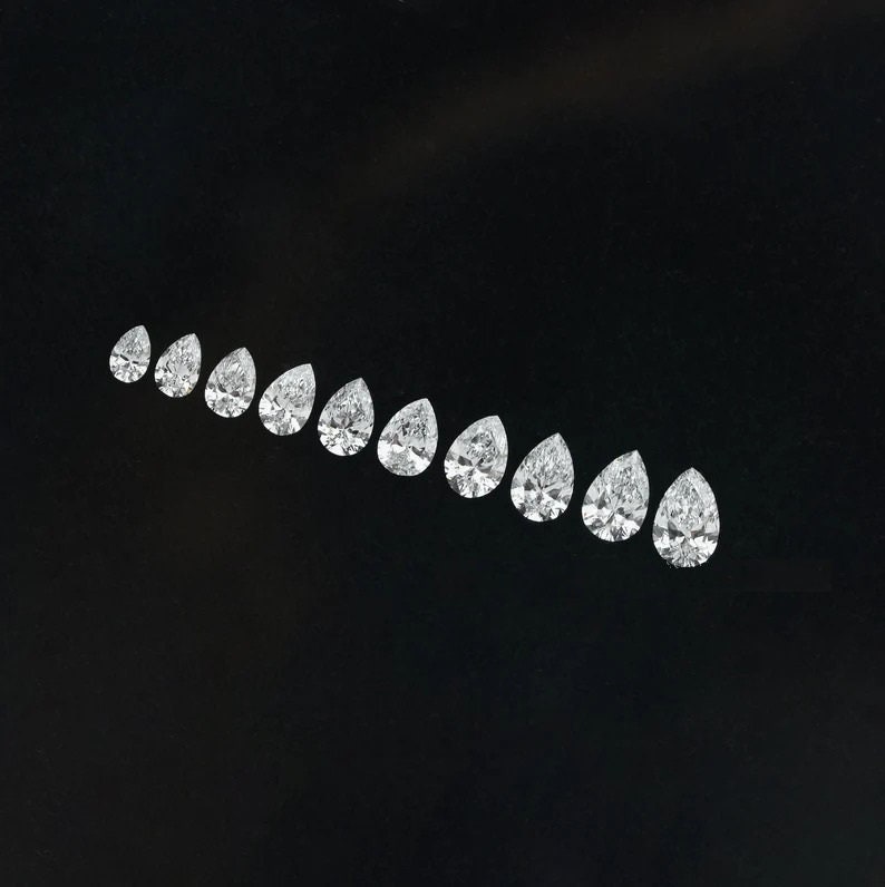 May include: A row of pear-shaped diamonds arranged in a graduated size order, from smallest to largest, on a black background.