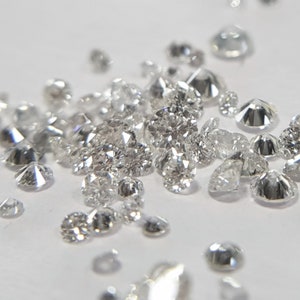 May include: A collection of loose, clear, faceted diamonds of various sizes, scattered on a white surface.